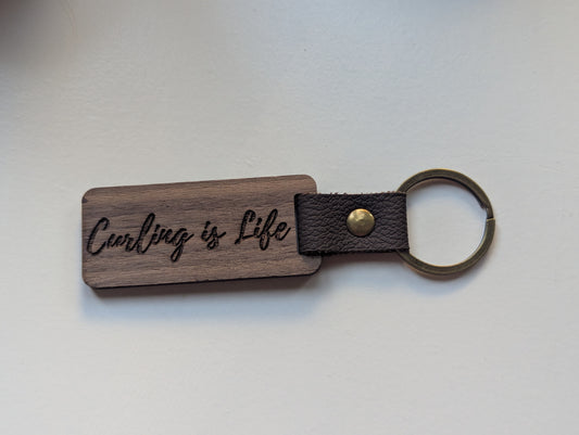 Wooden keychain with leather strap and 'Carling is Life' engraving on a light background