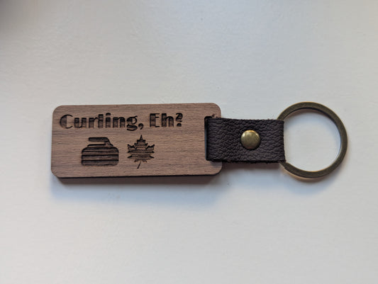 Wooden keychain with leather strap and 'Curling, Eh?' text on a white background
