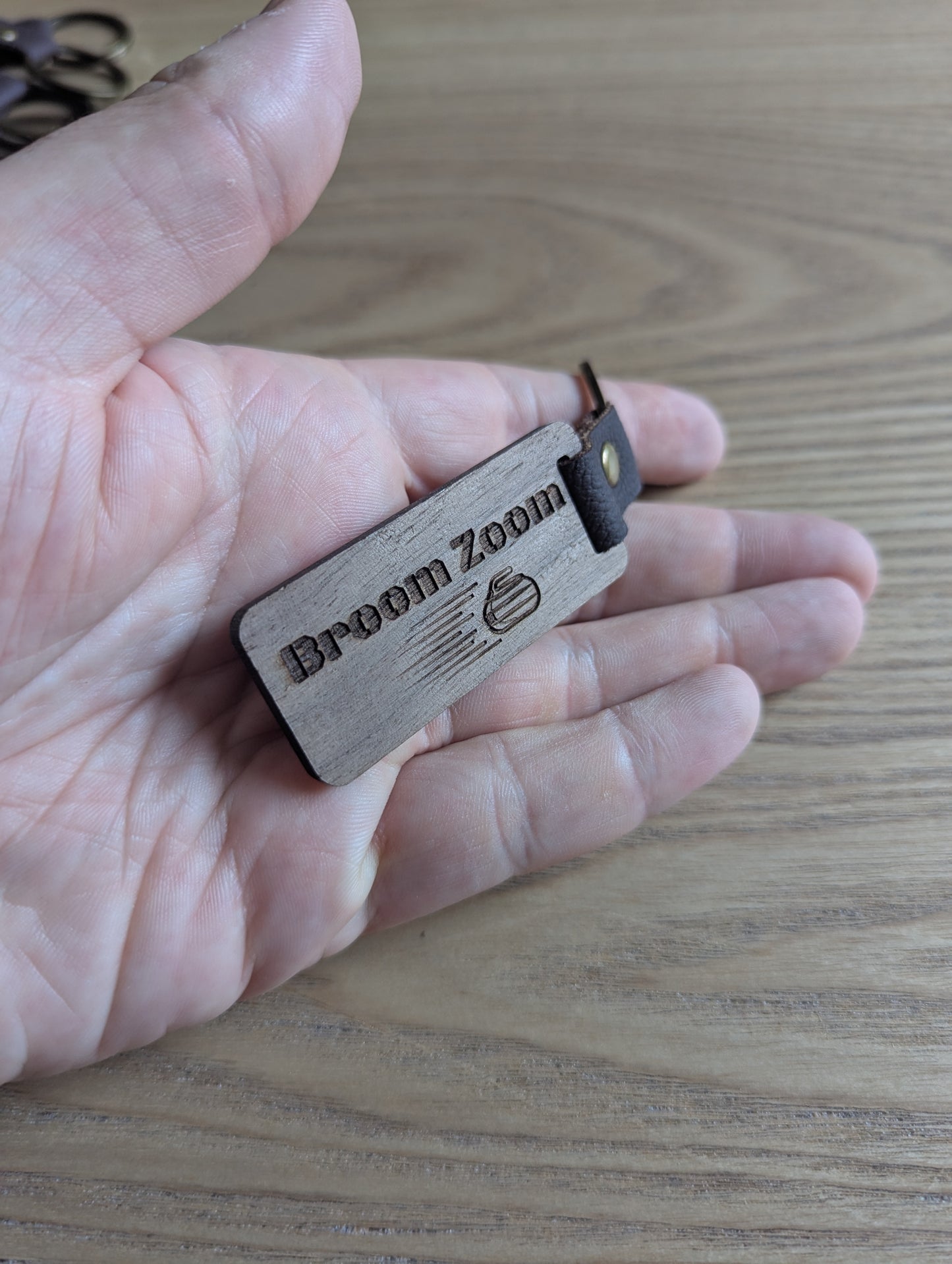 Wooden device labeled 'Broom Zoom' held in a hand on a wooden surface