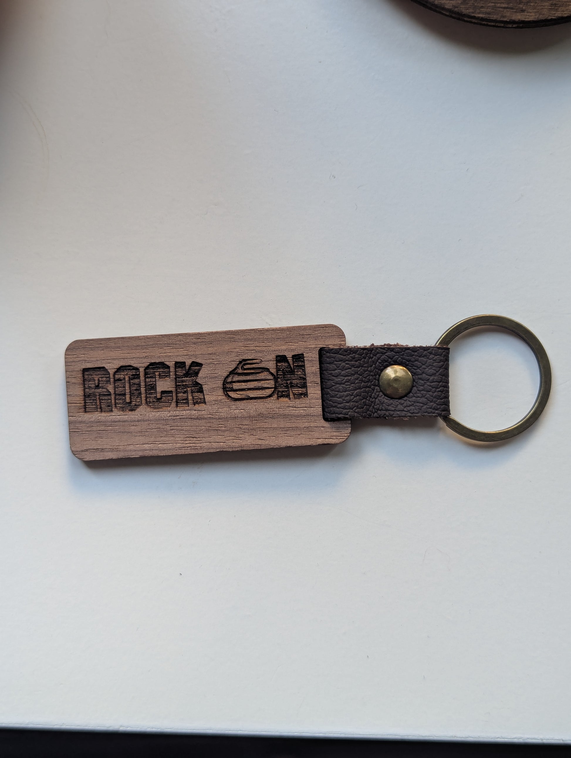 Wooden keychain with leather strap and 'Rock On' engraving on a white background