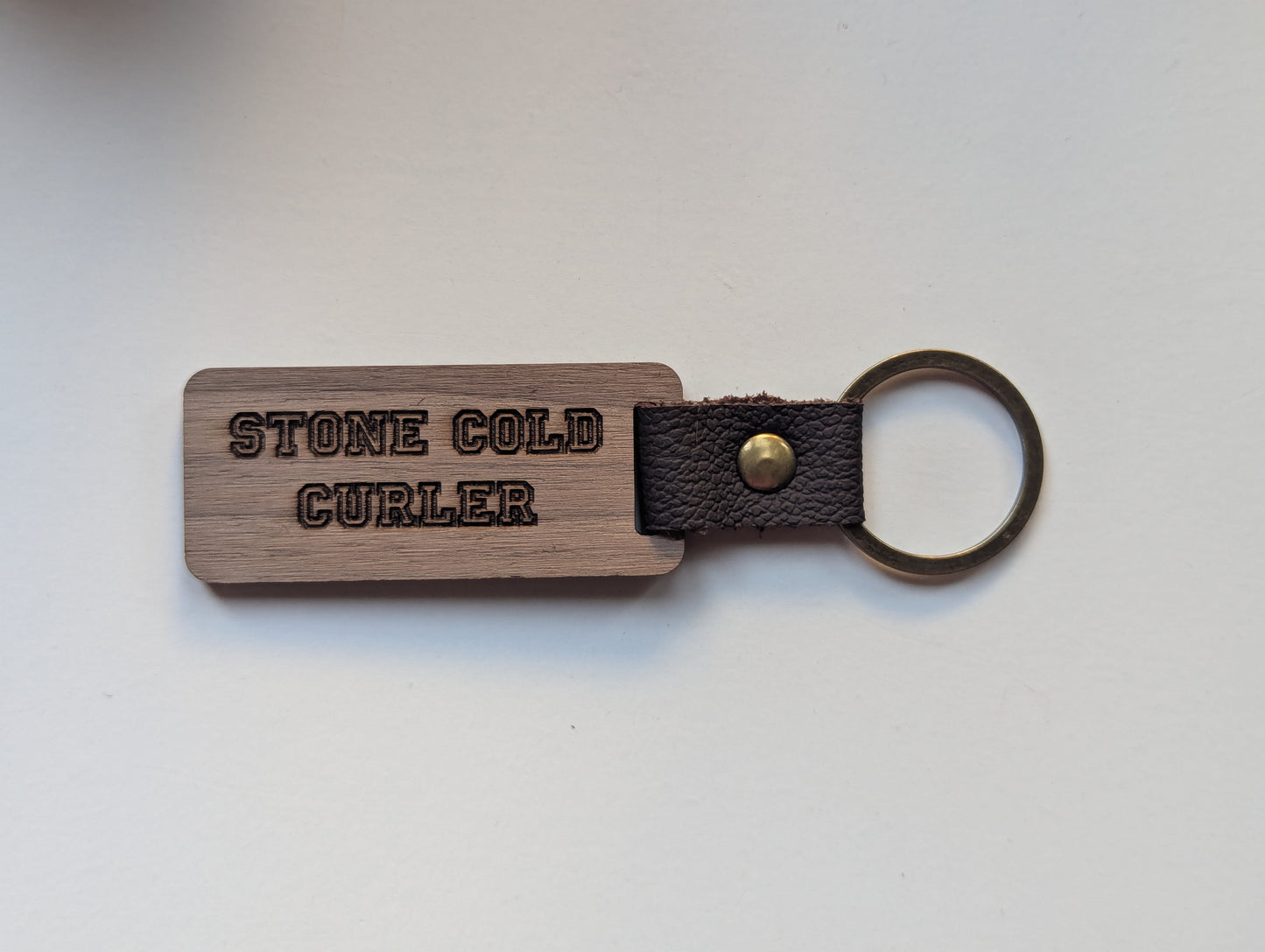 Wooden keychain with leather strap and 'STONE COLD CURLER' engraving on a light gray background