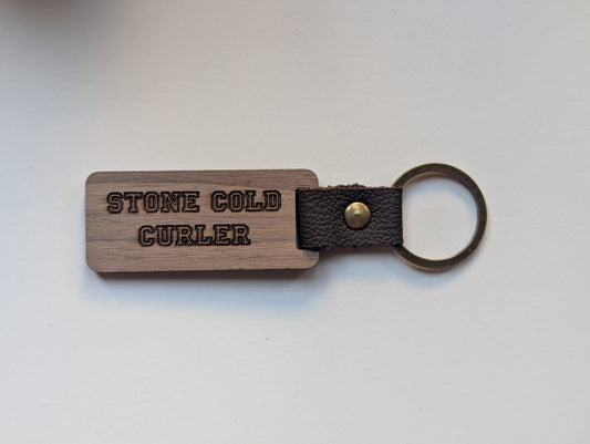 Wooden keychain with leather strap and 'STONE COLD CURLER' engraving on a light gray background