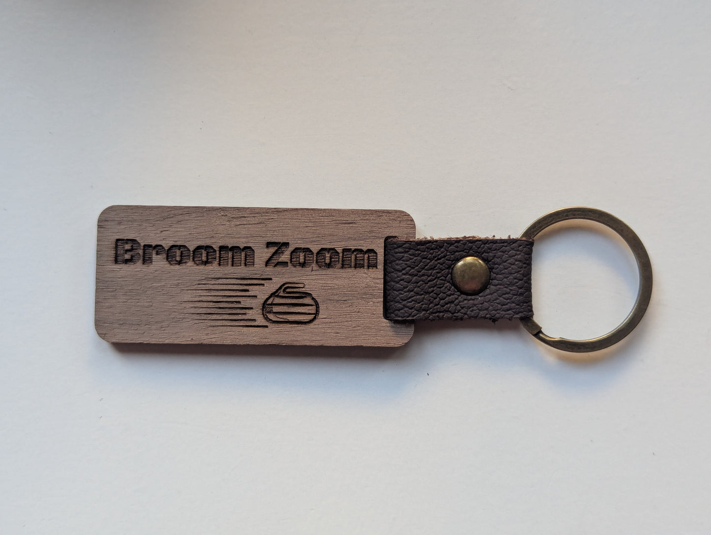 Wooden keychain with leather strap and 'Broom Zoom' branding on a white background