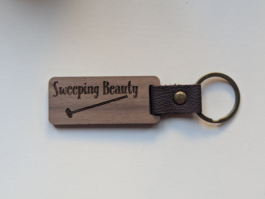 Wooden keychain with leather strap and engraved text on a white background