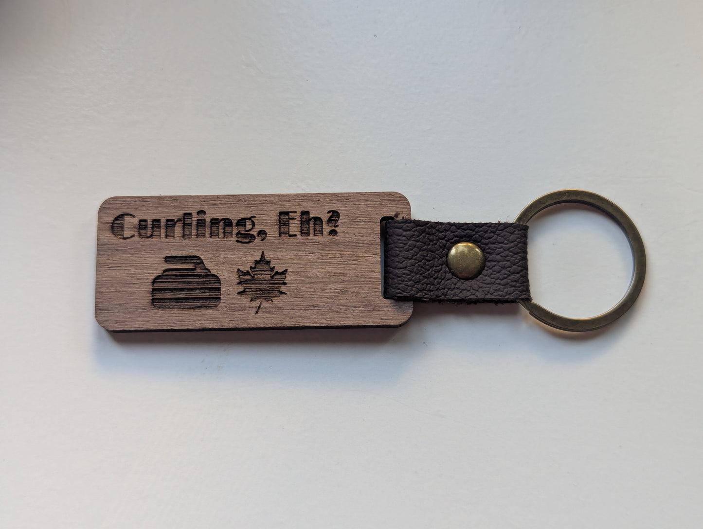 Wooden keychain with leather strap and 'Curling, Eh?' text on a white background