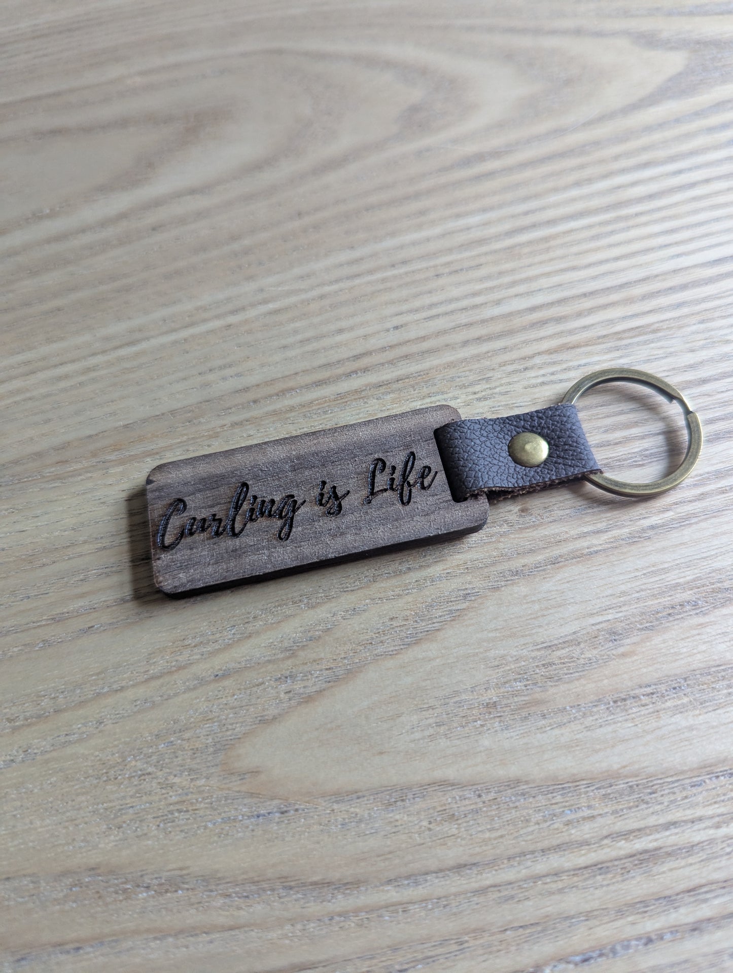Keychain with 'Curling is Life' engraving on a wooden surface