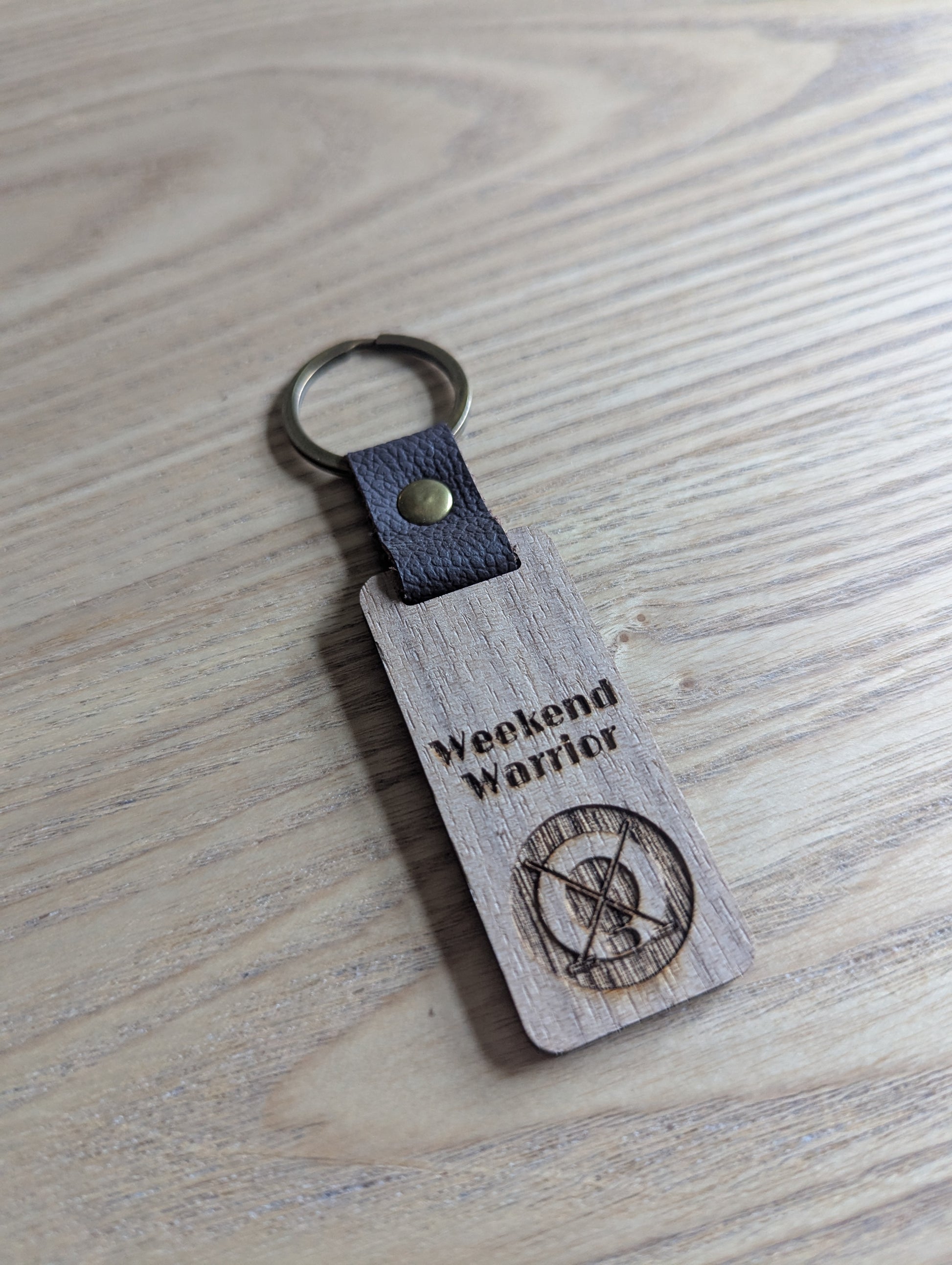 Wooden keychain with leather strap and 'Weekend Warrior' engraving on a wooden surface