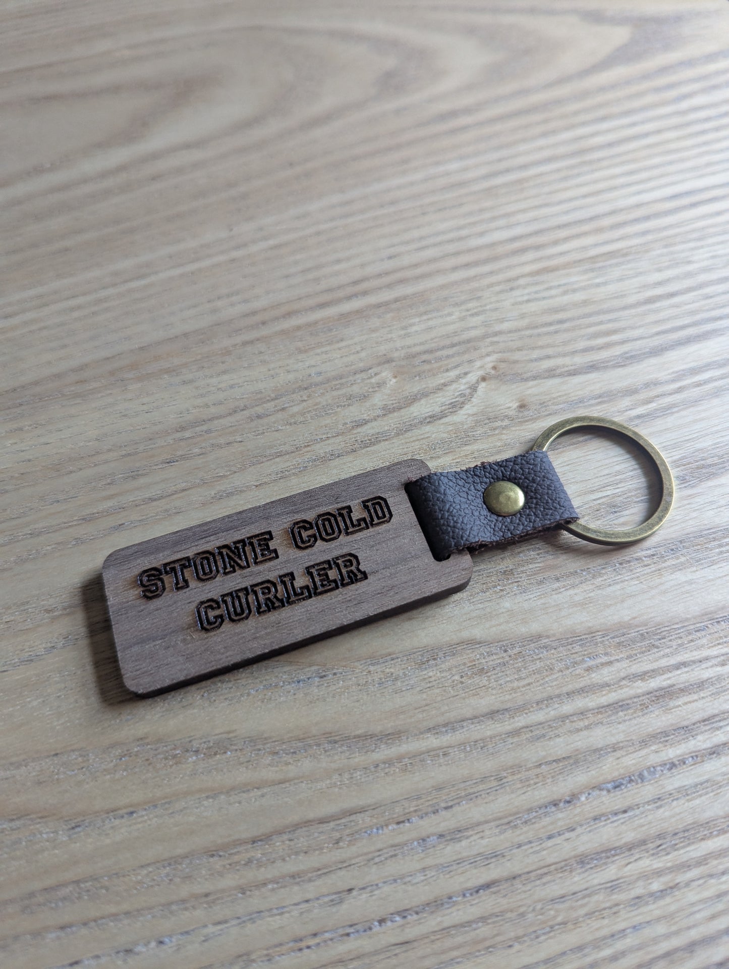 Keychain with 'STONE COLD CURLER' engraving on a wooden surface