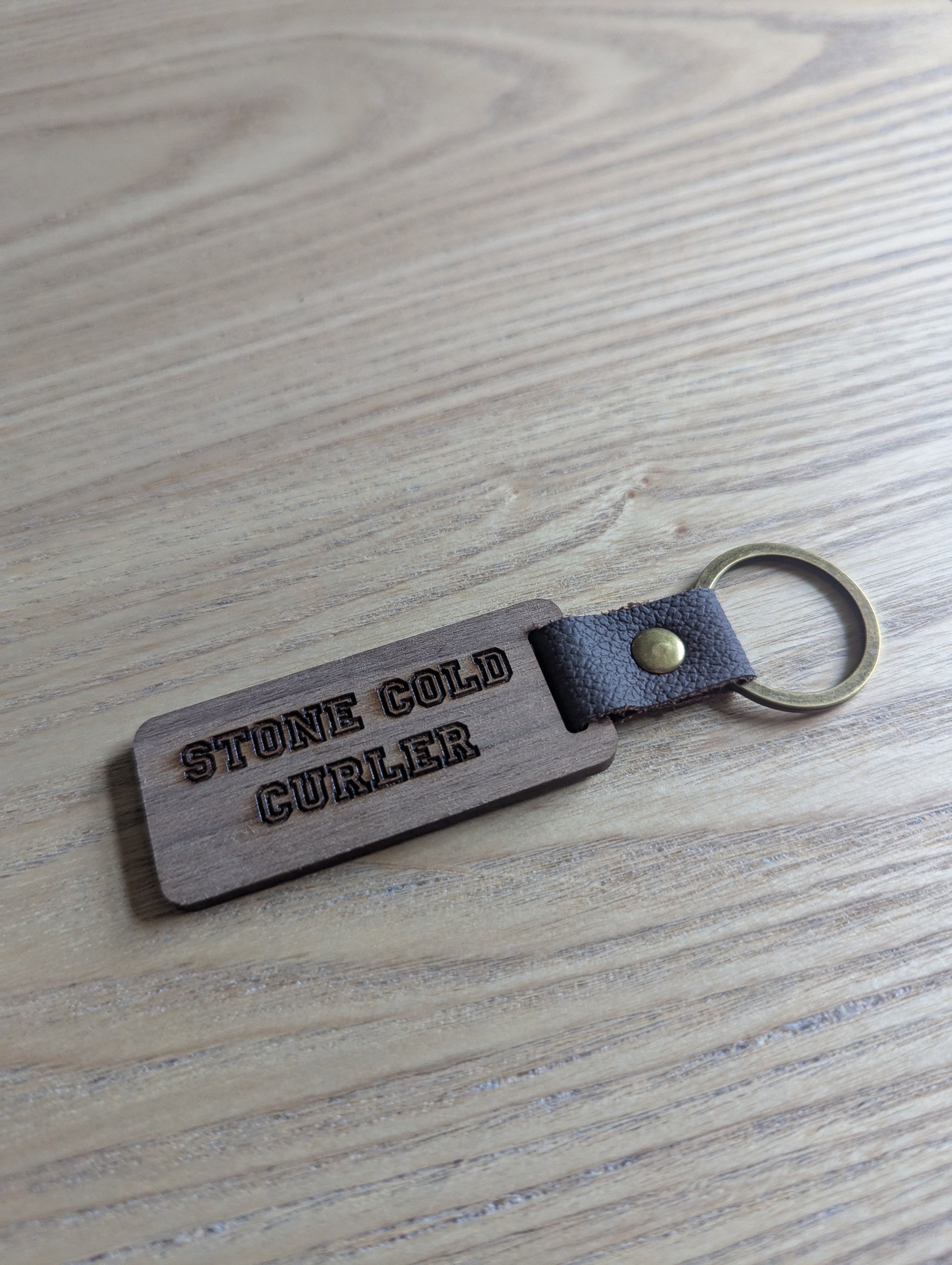 Keychain with 'STONE COLD CURLER' engraving on a wooden surface