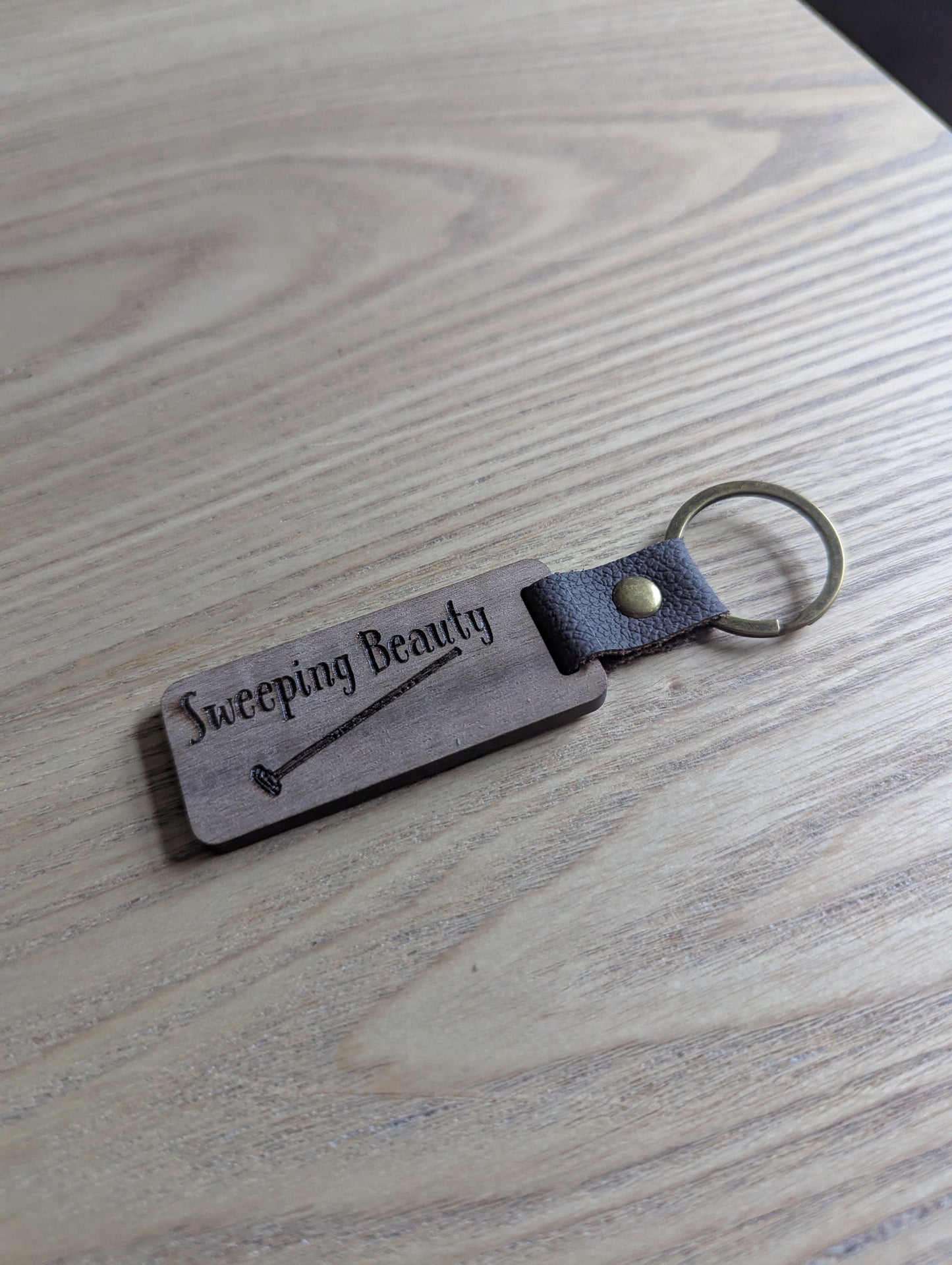 Keychain with 'Sweeping Beauty' engraving on a wooden surface