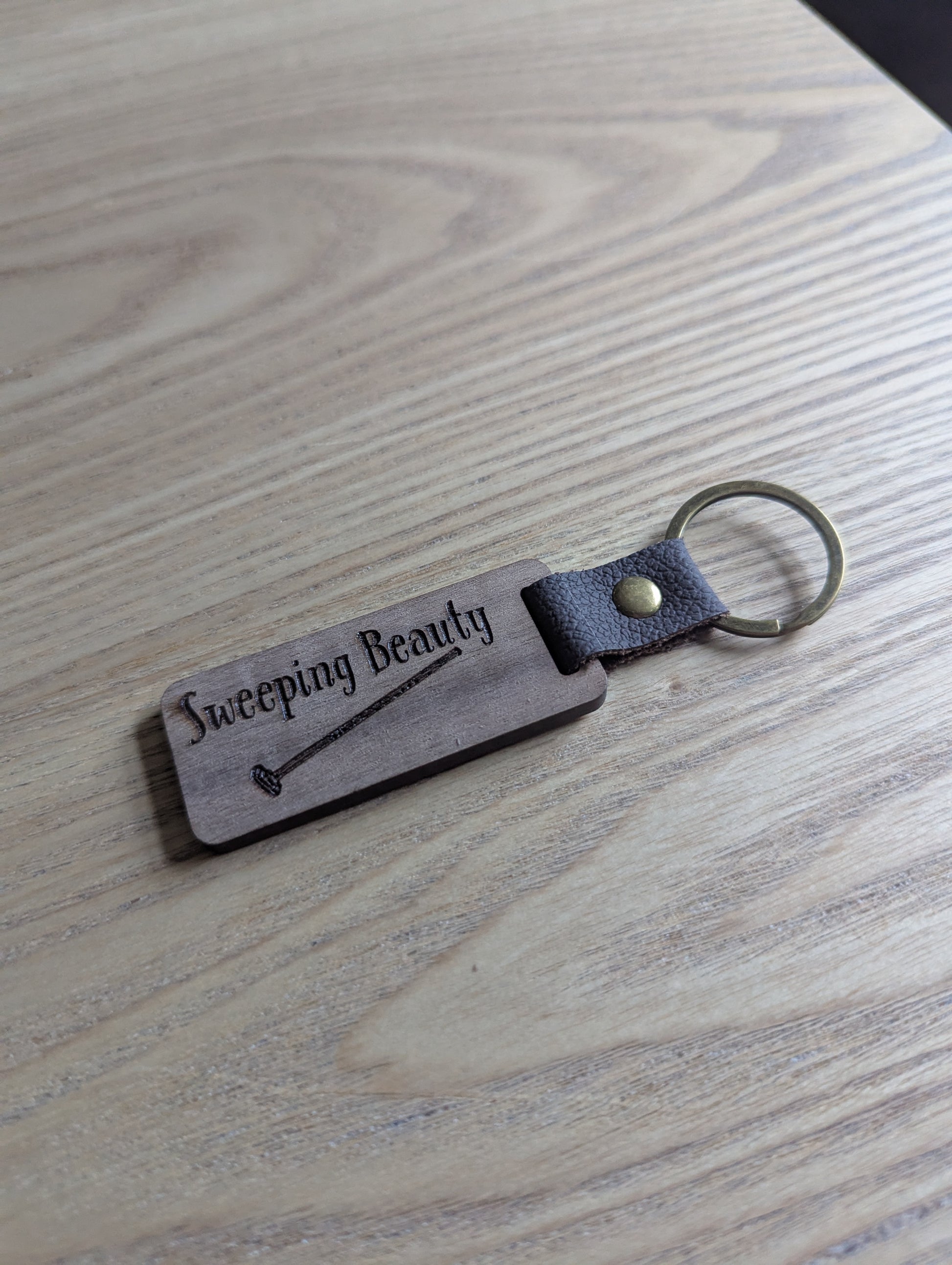 Keychain with 'Sweeping Beauty' engraving on a wooden surface
