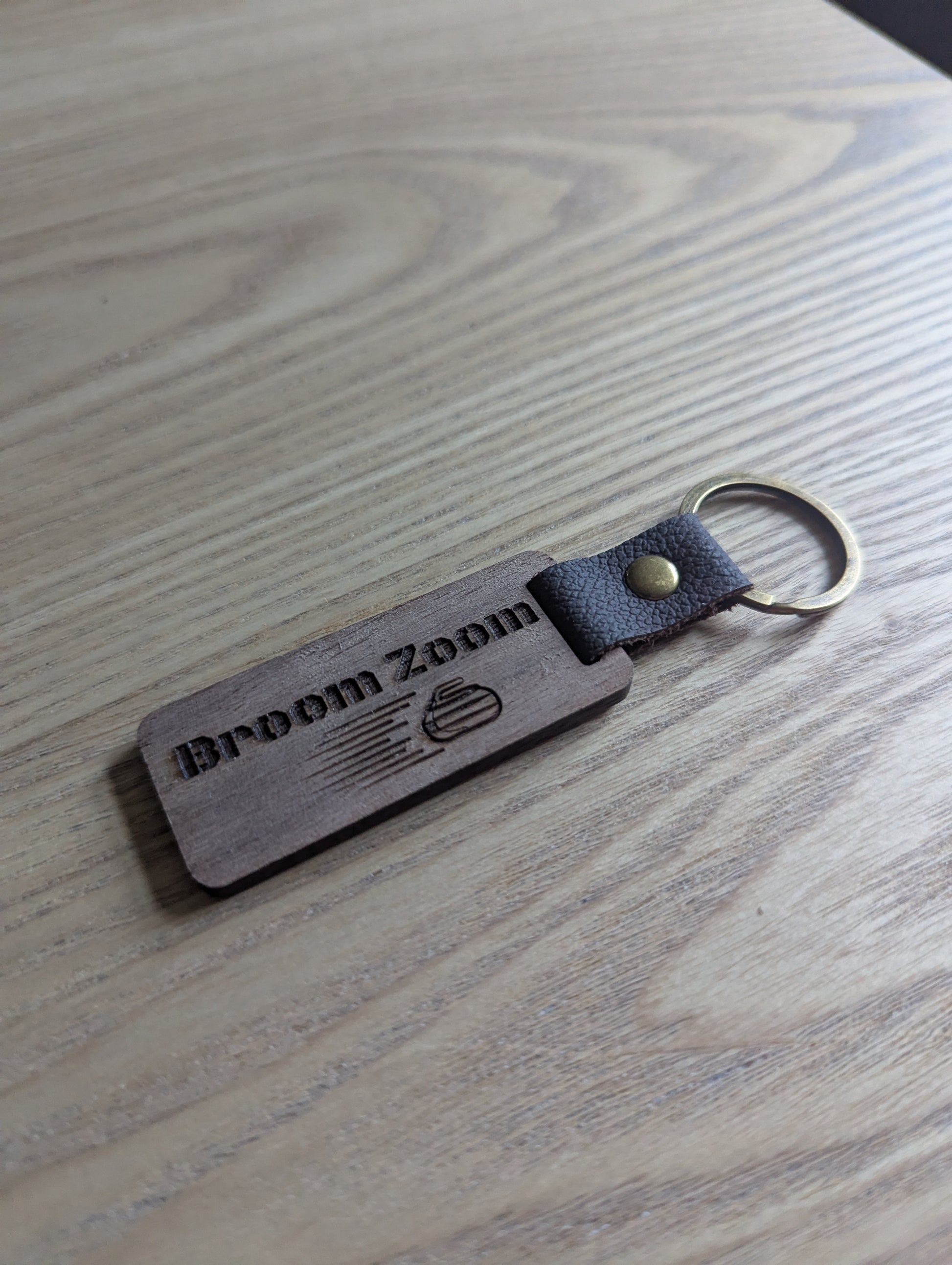 Wooden keychain with 'Broom Zoom' branding on a wooden surface