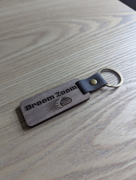 Wooden keychain with 'Broom Zoom' branding on a wooden surface