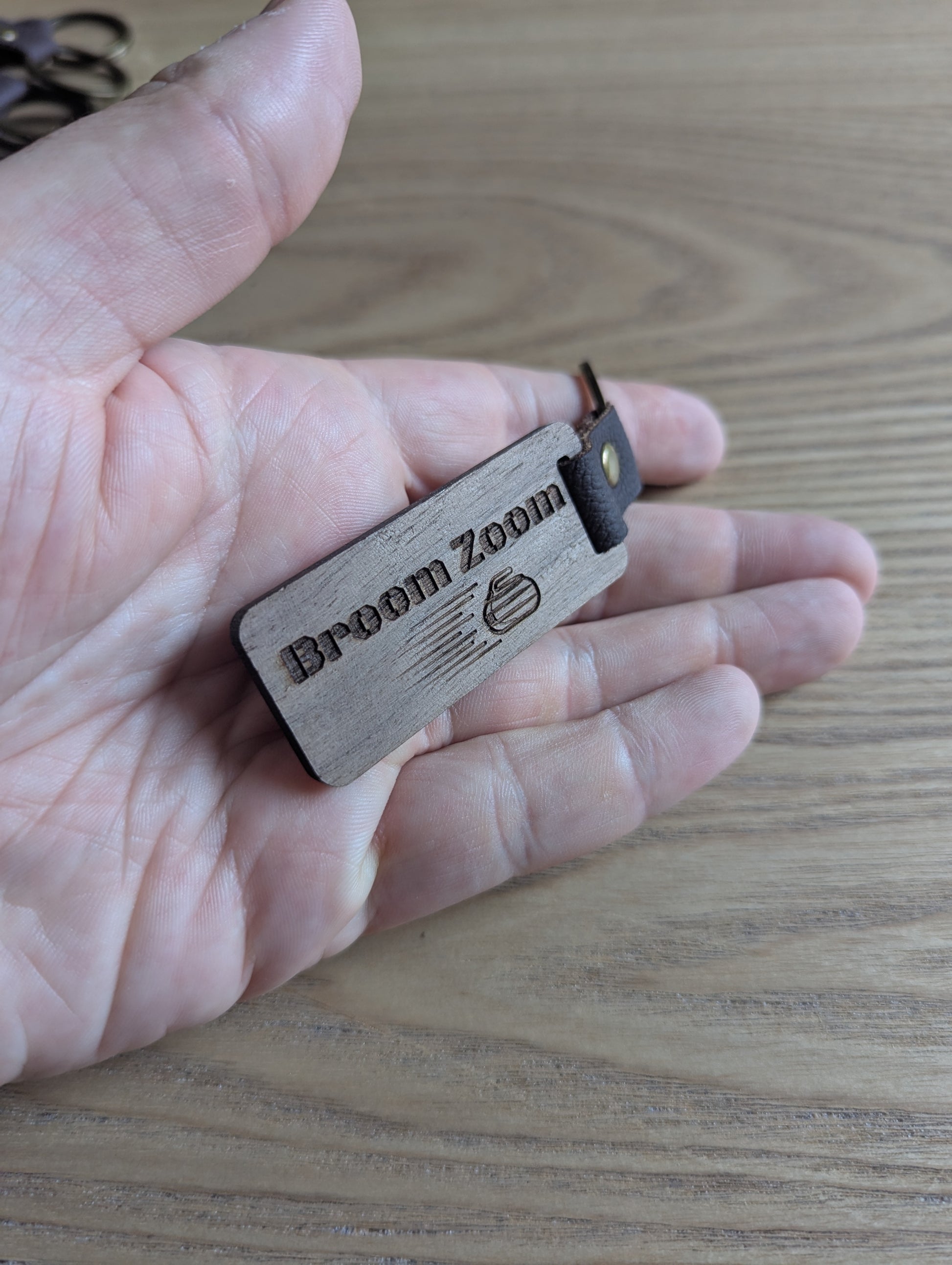 Wooden device labeled 'Broom Zoom' held in a hand on a wooden surface