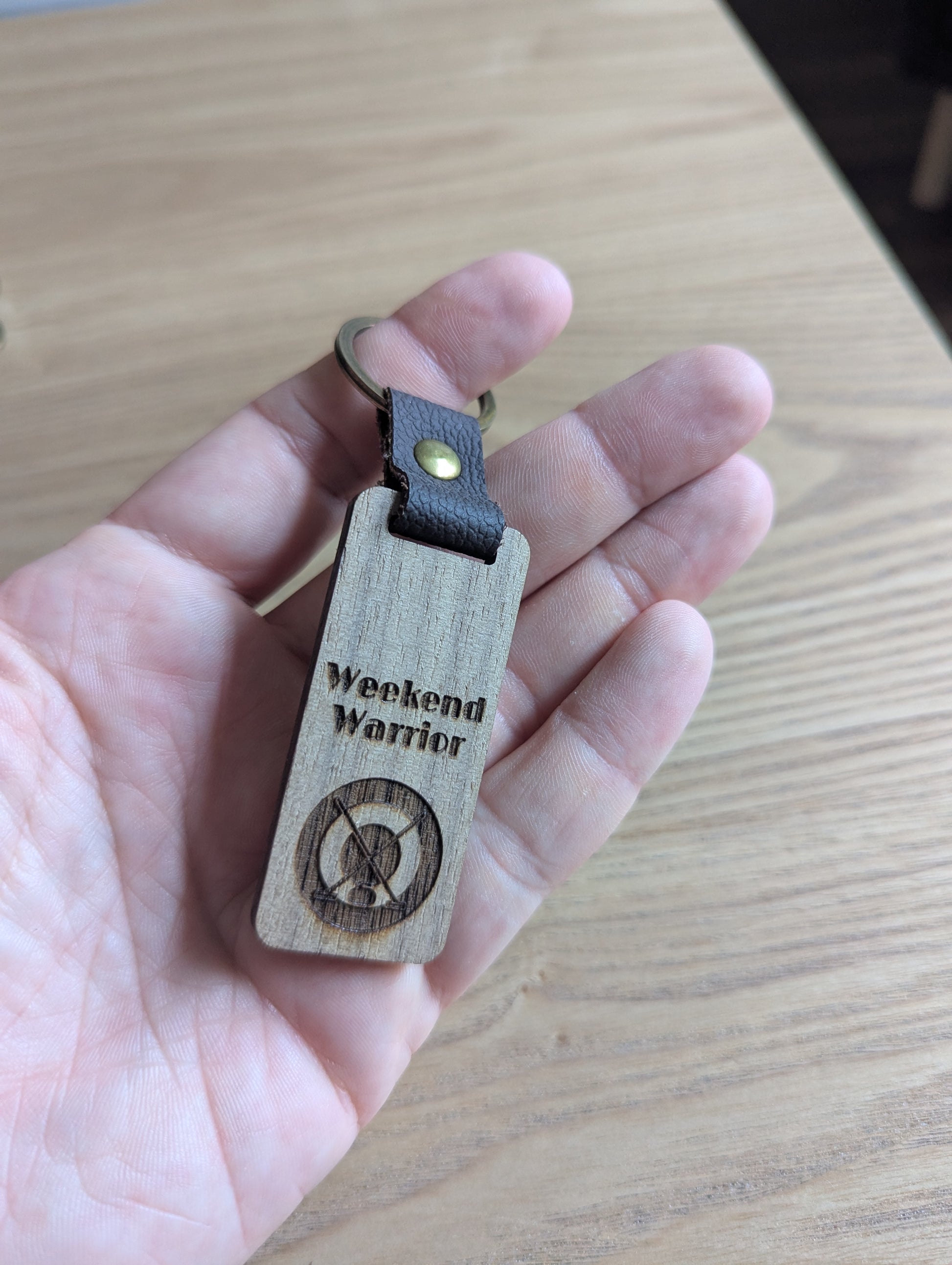 Wooden keychain with 'Weekend Warrior' engraving held in a hand on a wooden surface