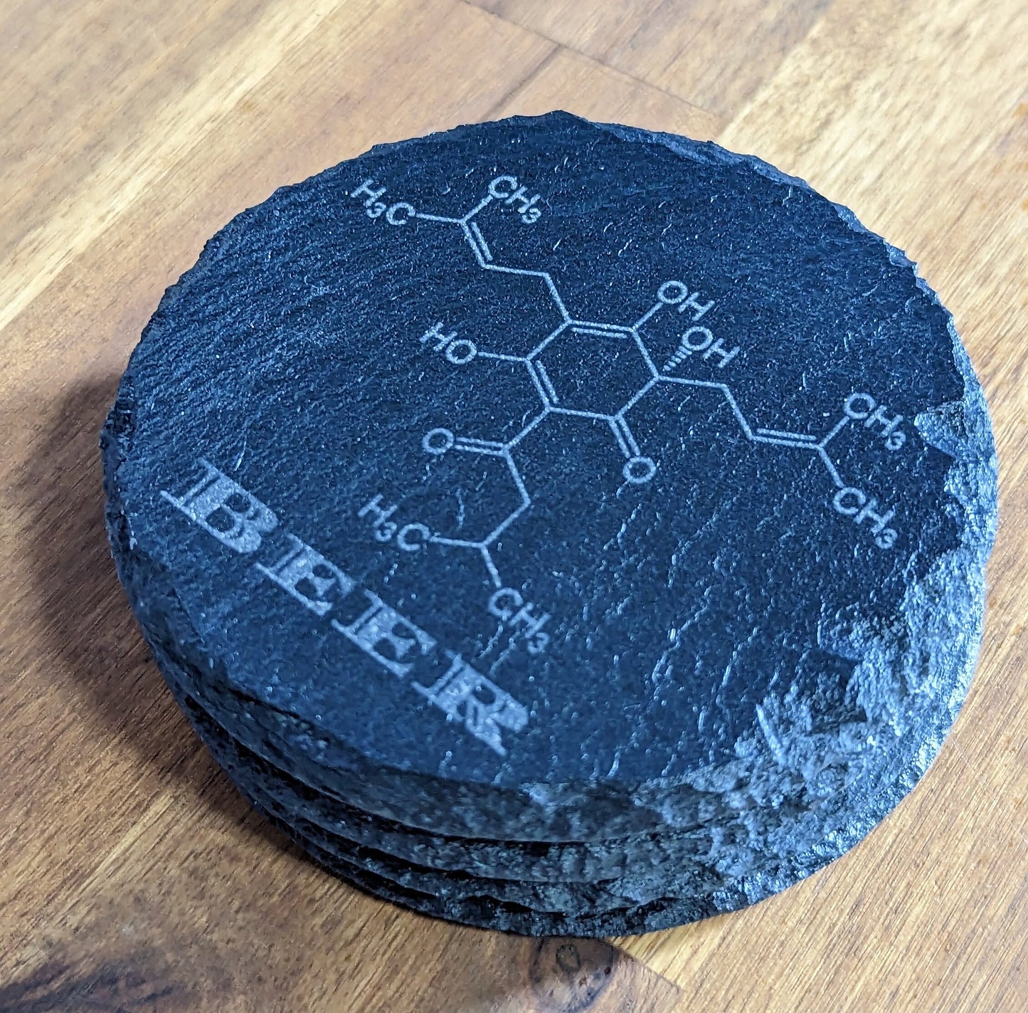 Set of 4 Charcoal Slate Coasters with Beer Molecule Etching on a wooden table.